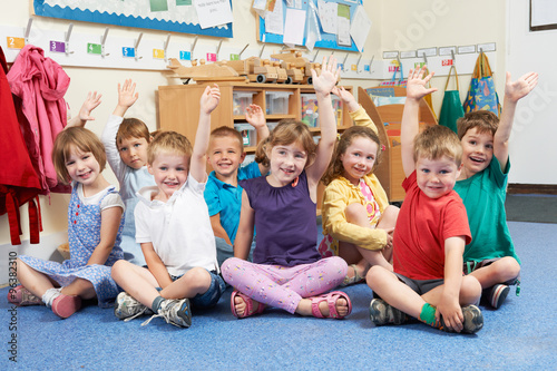 Group Of Elementary School Pupils Putting Hands Up In Class