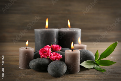 Alight wax grey candles with roses and pebbles on wooden background - relax concept