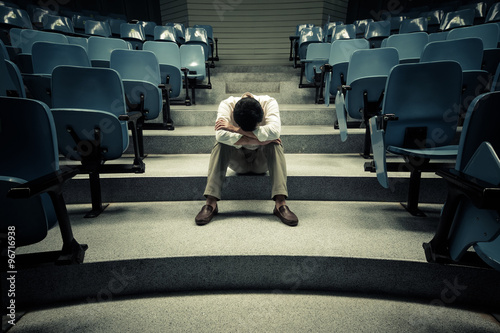 Businessman sitting desperately in the middle of the stair path with rows of chairs along both sides