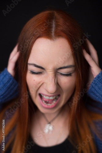Young woman screaming at black background. Girl having headache.
