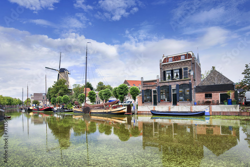 Smooth green canal with moored boats and monumental houses in the old town of Gouda, The Netherlands.