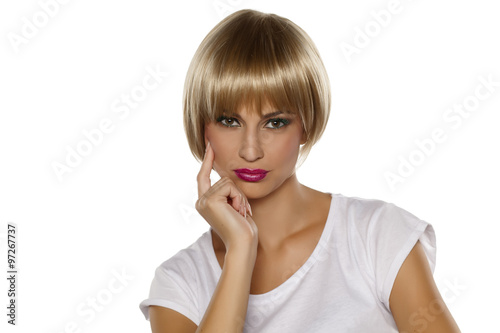 Serious young woman with short blonde wig posing on a white