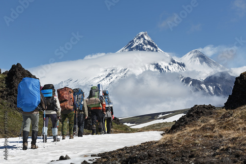 Group of hikers goes in mountain on background volcanos