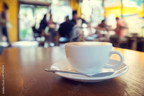 Cup of coffee on table in cafe with people - shallow depth of field
