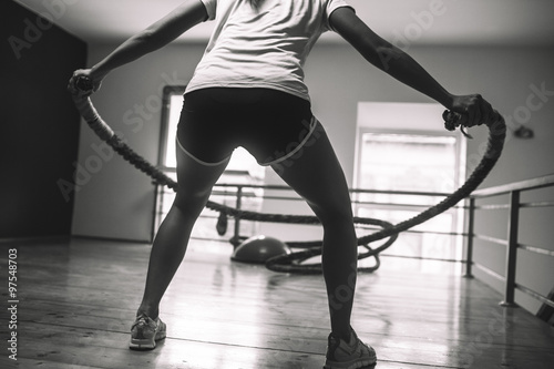 A determined female gym-goer works up a sweat while energetically using battle ropes, pushing her limits to build strength and improve her overall fitness.