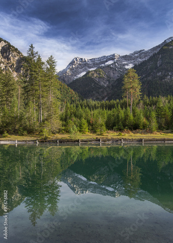 Die Bergketten der Tiroler Alpen spiegeln sich auf der glatten Oberfläche des Plansees in Österreich. 
