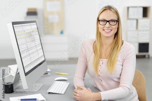 motivierte mitarbeiterin sitzt am schreibtisch im büro mit tabellen auf dem monitor