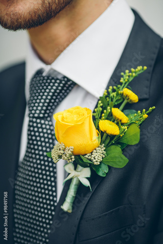 groom's hand arranging yellow boutonniere flower on suit