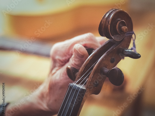 Old man luthier hands tuning aged violin 