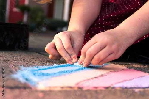 Kid playing with colored chalk on the sidewalk. Nice colors in the golden hour. Close up of the hands.