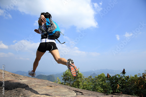 young asian woman hiker running on mountain peak cliff