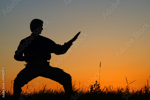 Man practicing karate on the grassy horizon after sunset. Art of self-defense. Silhouette against a bright orange sky.
