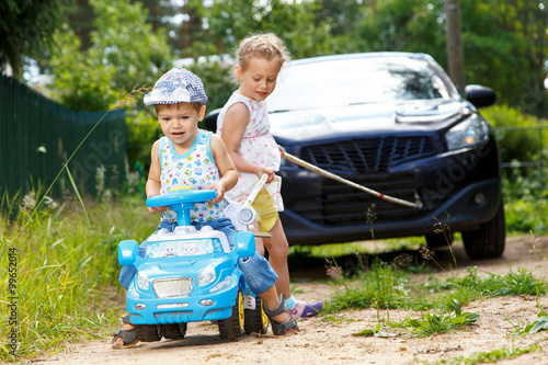 Two kids try to tow real automobile with the help of toy car