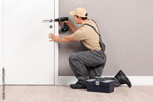 Young locksmith installing a lock on a door