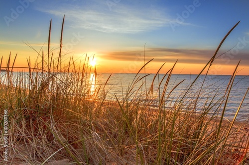 Dawn Of A New Day.Beautiful sunrise illuminates sand dunes and the blue water horizon as a new day begins. Port Austin, Michigan.