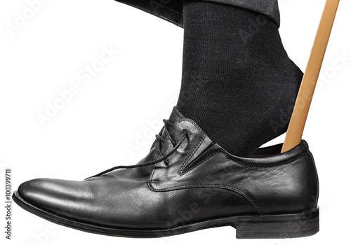 man puts on black shoe with shoehorn isolated