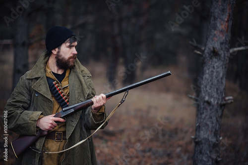 brutal hunter, bearded man in warm hat with a gun in his hand