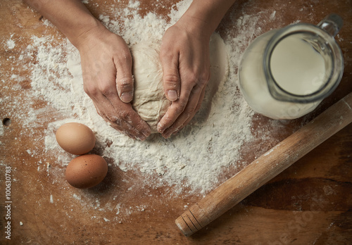 Close-up of baker hands kneading cake dough on the board with flour, eggs and milk. Baking concept.