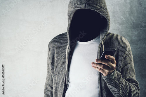 Faceless hooded person using mobile phone, identity theft concep