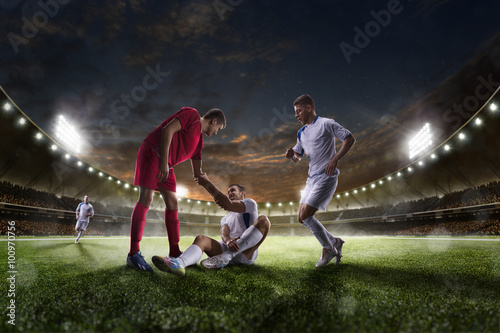 Soccer player helps onother one on sunset stadium background panorama