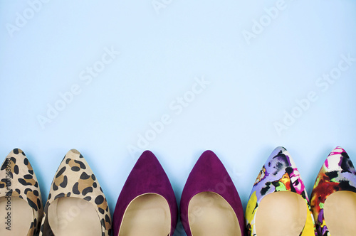 Stiletto shoes in different colours and patterns in straight line on light blue background.