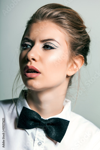 Beautiful young woman wearing a shirt and bow tie against a gray background