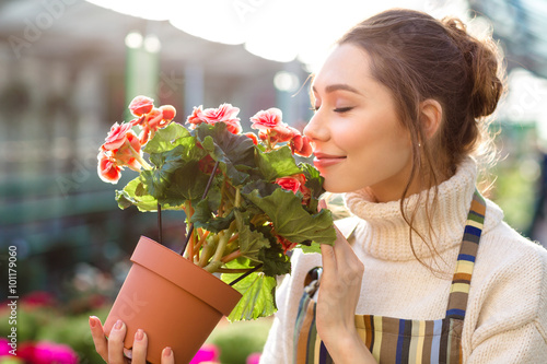 Inspired woman florist smelling flowers of begonia in greenhouse