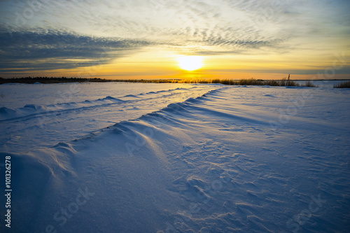 Bright sun sunset winter with road and footprints in the snow.