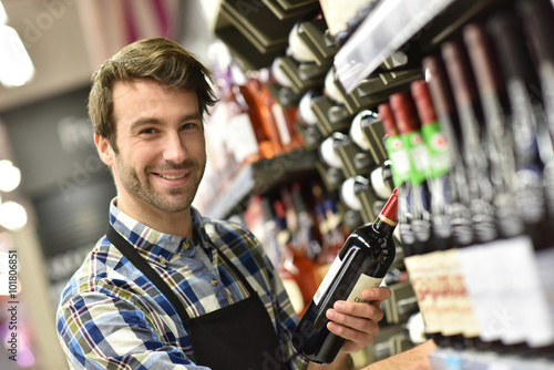 Wine specialist putting bottle up in winery section of supermarket