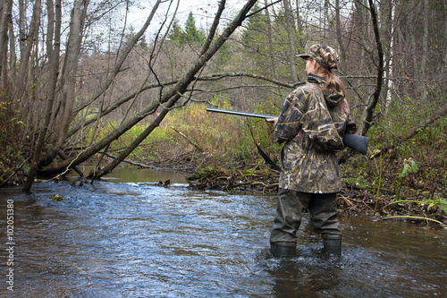 woman hunter in waders crossing the forest river