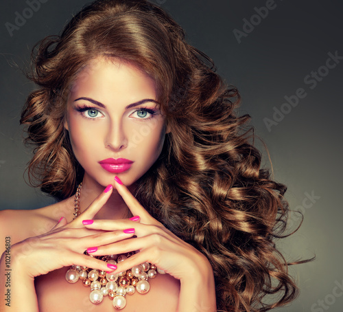 Beautiful model brunette with long curled hair . Hairstyle wavy curls . Crimson nails manicure .Makeup color fuchsia . 