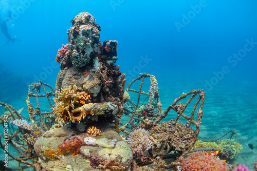 Buddha statue on sea sand bottom on background of snorkeler swimming deep down into water to observe tropical reef. Vacation adventures and underwater safari on scuba diving sites in Bali, Indonesia.