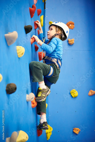 Little boy is climbing on blue wall