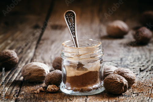 Ground nutmeg in a jar and whole nuts on an old wooden backgroun