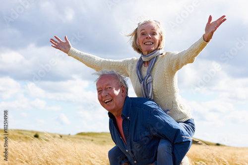Senior Man Carrying Senior Woman On Walk In Countryside