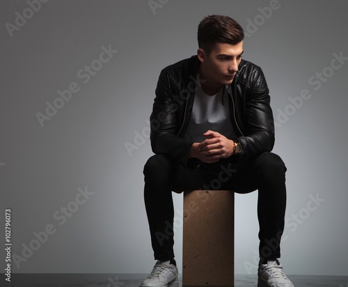 young man in black leather jacket posing seated in studio