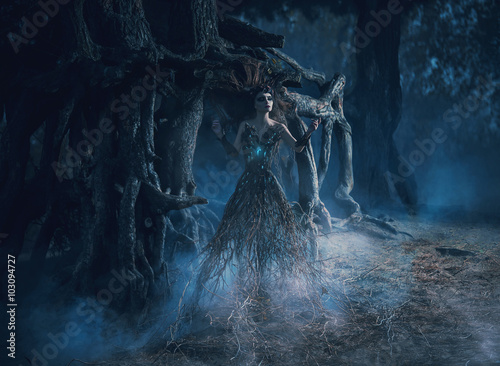 fantasy woman trees spirit wanders woods in dark magic forest. girl tree took root near mighty old oak, mystical gothic blue image, spells, fashion model. creative dress costume. color toning