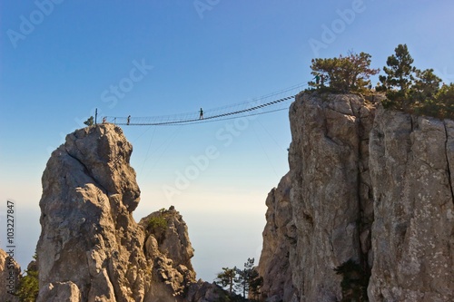 People crossing the chasm on the hanging bridge. Black sea background, Crimea, Russia