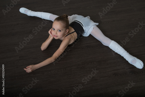 A little adorable young ballerina doing stretching exercises on