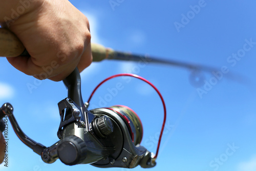 fisherman holding rod and reel under blue sky, selective focus