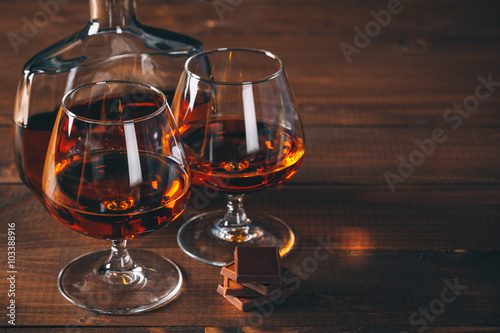 Two glasses of cognac and bottle on the wooden table.