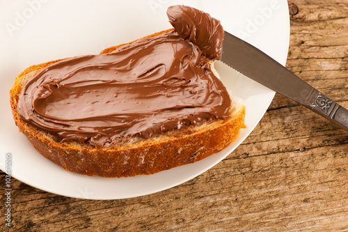 Slice of bread with sweet chocolate nougat spread on white plate