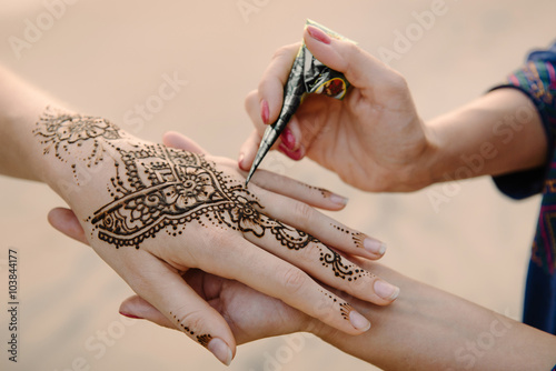 applying henna tattoo on women hands