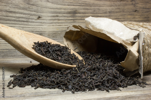 Dry tea leaves for black tea and wooden spoon on wooden background