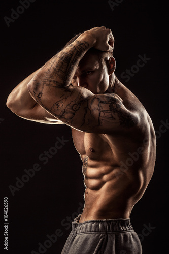 Muscular guy with tattooes holding his head. Isolated on grey background