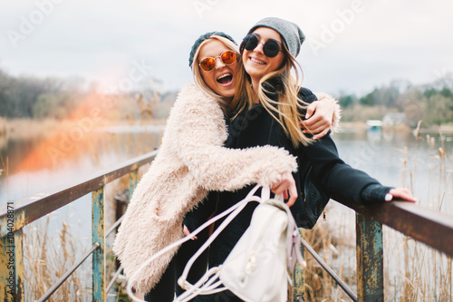 Outdoor lifestyle portrait of two best friends, smiling and having fun together, enjoy each other company posing and making selfie pictures to each other and share happiness 