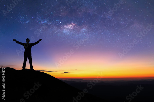 Silhouette of man is standing on top of mountain and spreading hand.