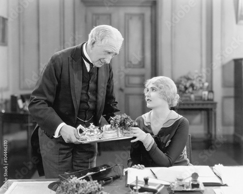 Older man serving a woman tea on a tray 