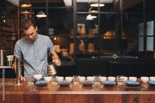 Barista preparing coffee tasting with rows of cups and beans