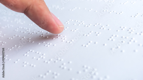 Finger read braille text in white paper.